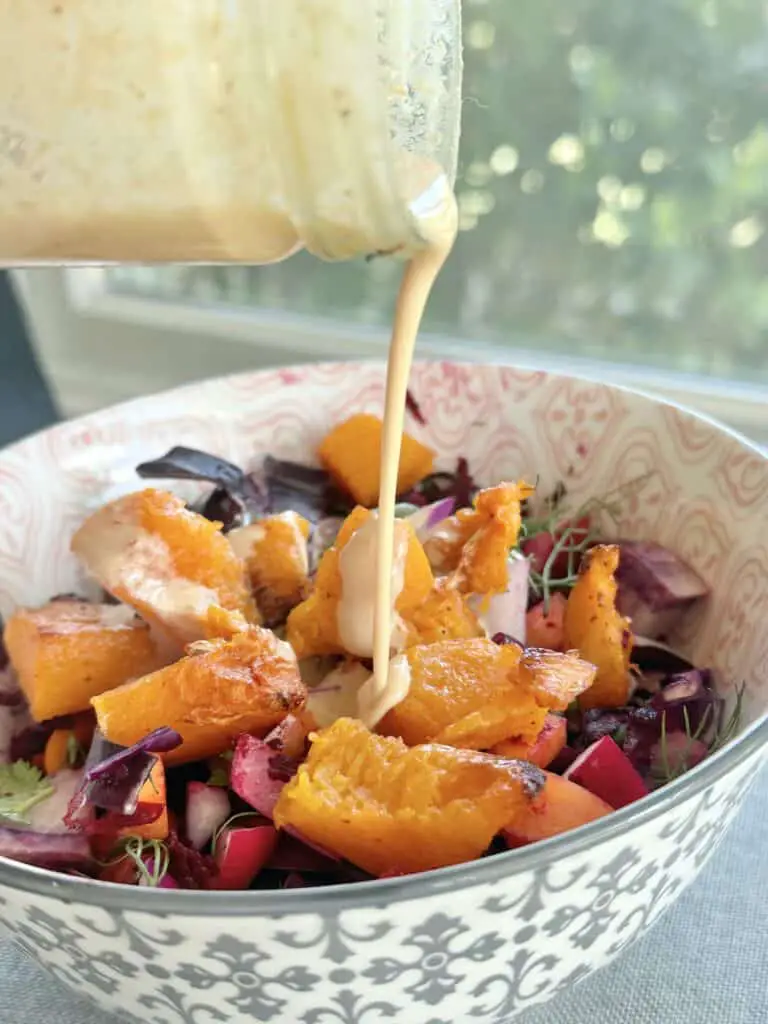 Pouring tahini dressing over squash bowl.