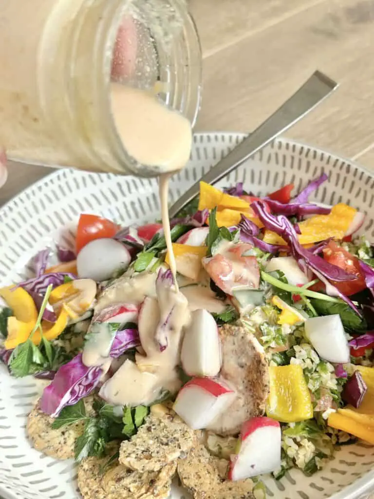 Pouring tahini dressing over colorful salad of radishes, cabbage, tomatoes, peppers, and more.
