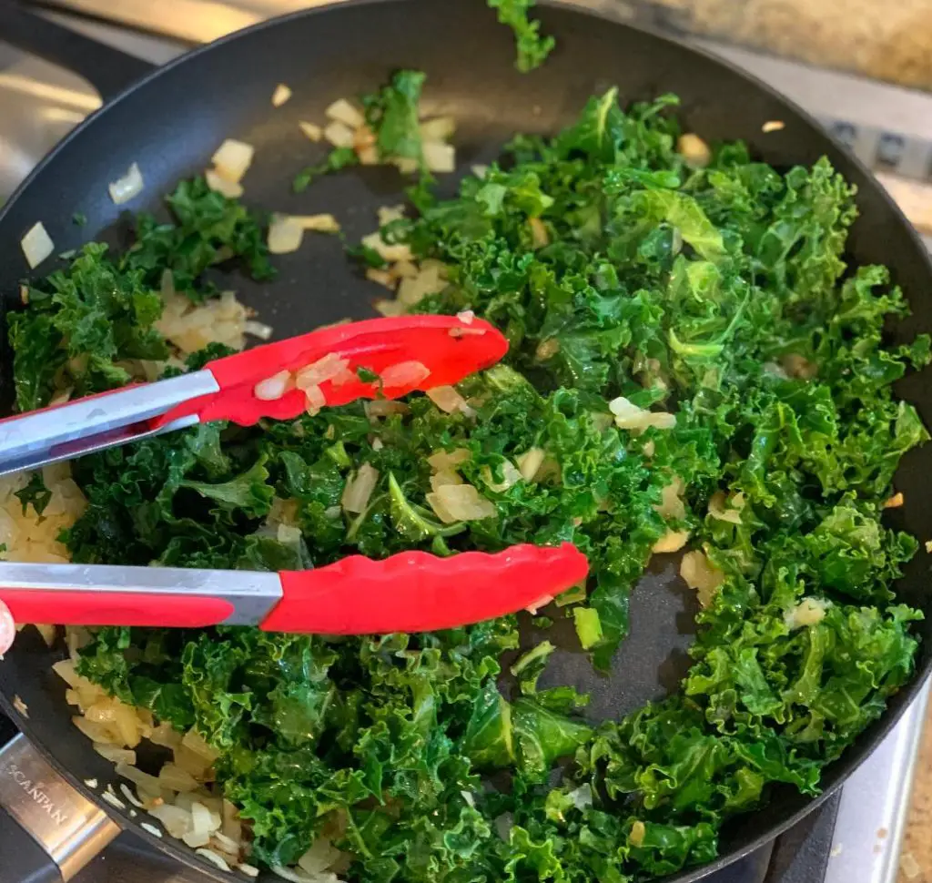 Using tongs to cook and move kale while wilting.