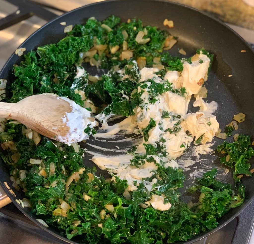 Adding in cream cheese to kale in pan.