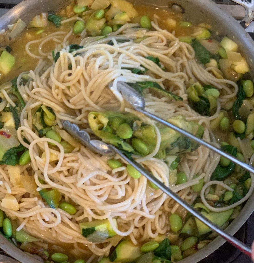Mix in spaghetti with tongs to your pasta with edamame.