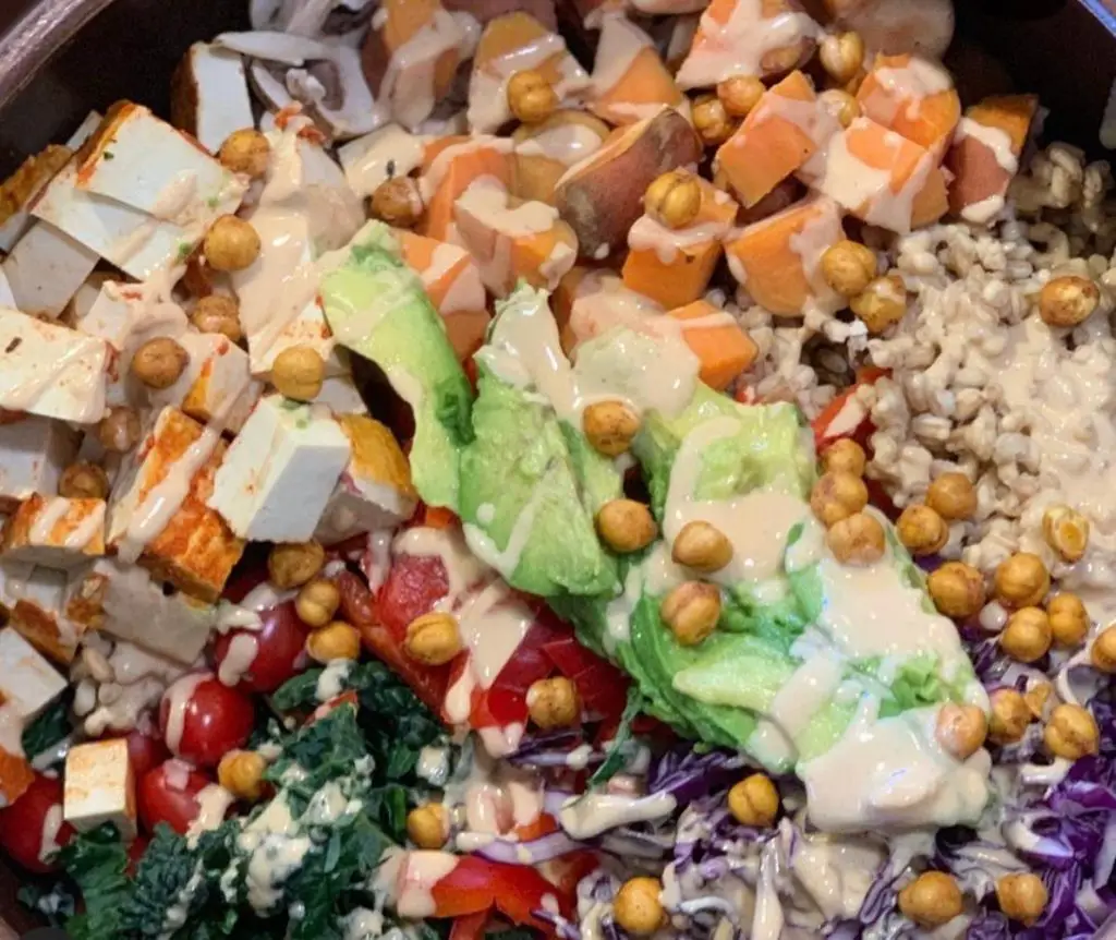 Rainbow salad filled with veggies, grains, beans, and tofu, with tahini dressing.