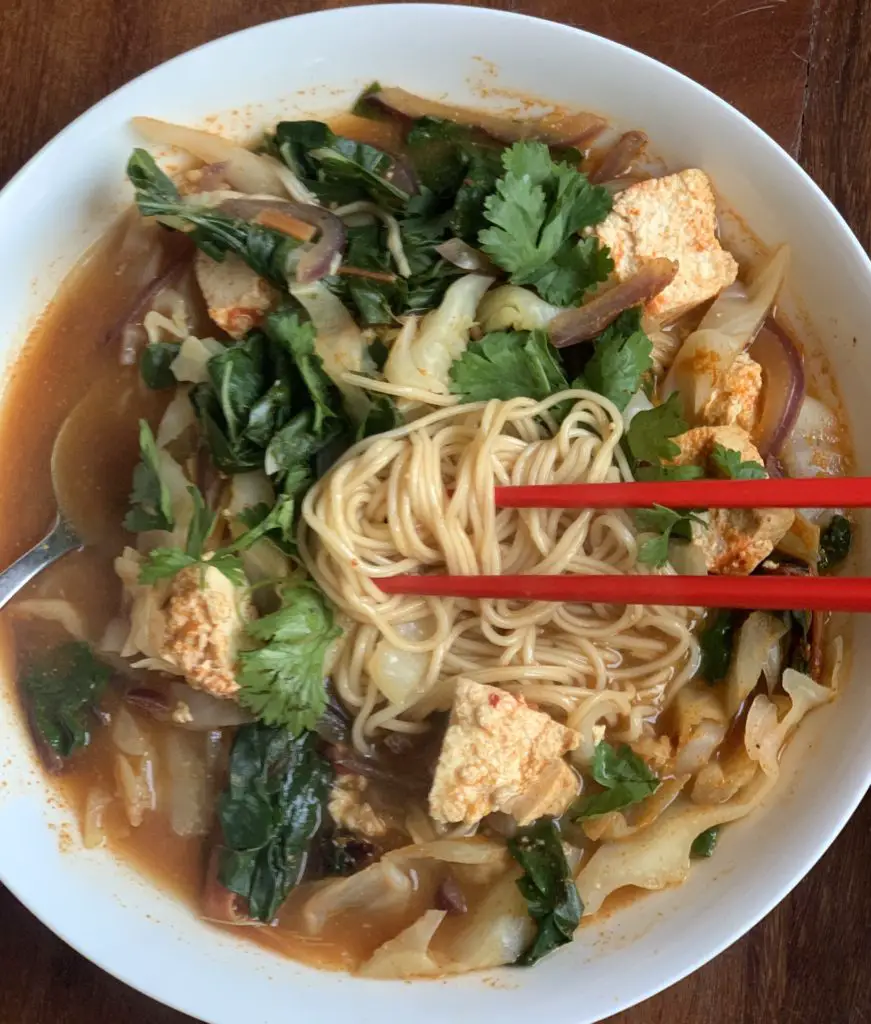 Bowl of spicy ramen with tofu and greens.