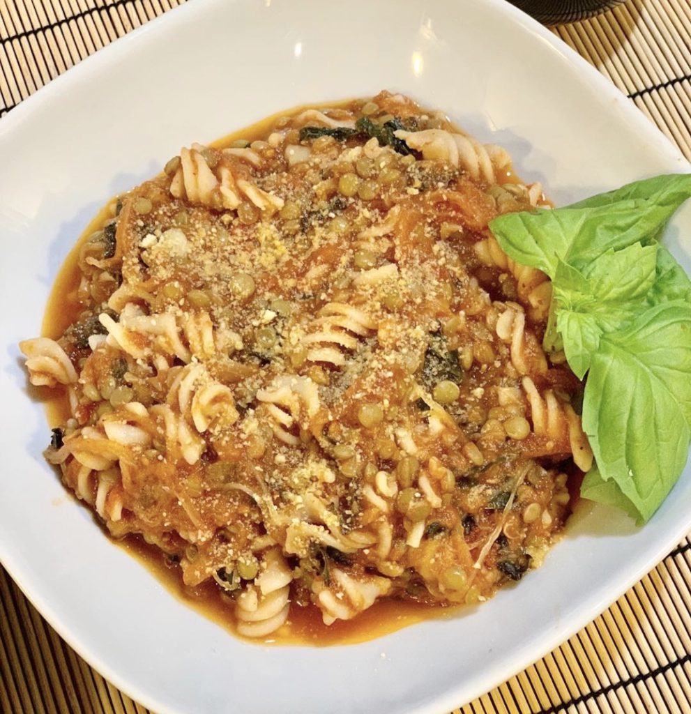 Bowl of hearty pasta garnished with basil in a white bowl.