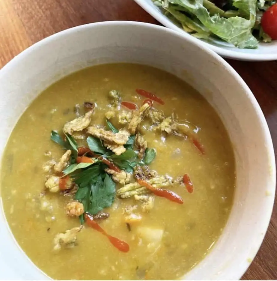 Split Pea soup topped with fried jalapeno pieces and herbs in white bowl. Salad on side.