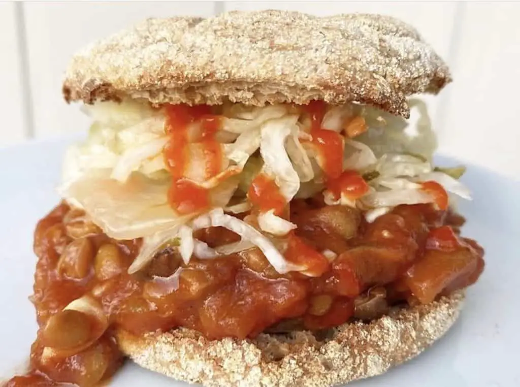 Lentil Sloppy Joe's shown messy on an English muffin with slaw and hot sauce.
