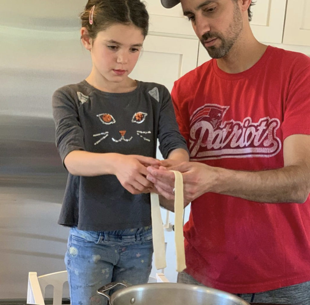 Girl helping her dad make noodles in her kitchen helper stool.