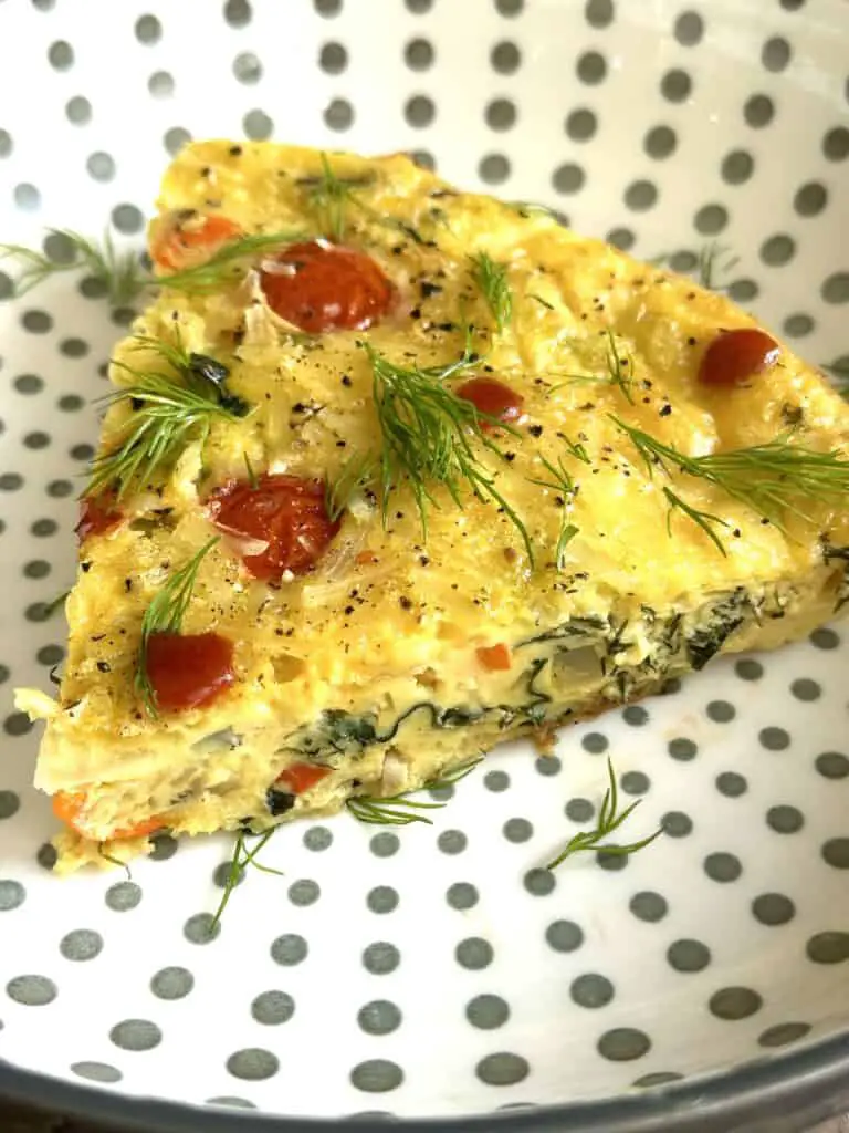 Gorgeous slice of vegan frittata on a polka dot plate, topped with sriracha and fresh dill.