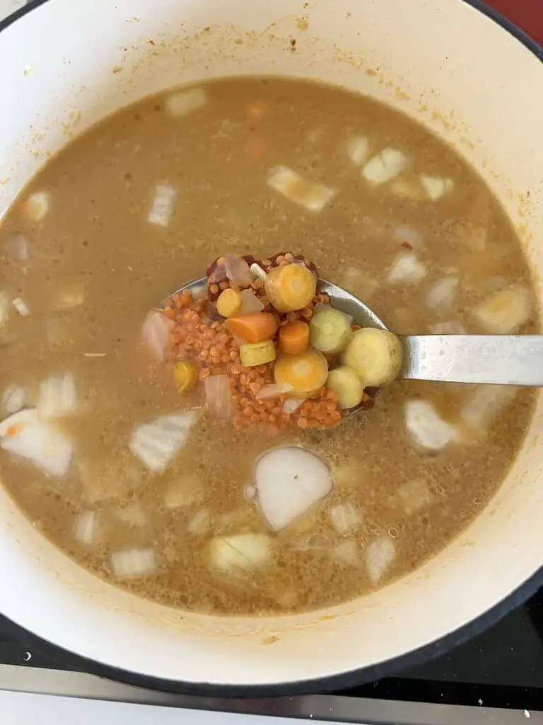 Cooking soup, spoon showing ingredients.