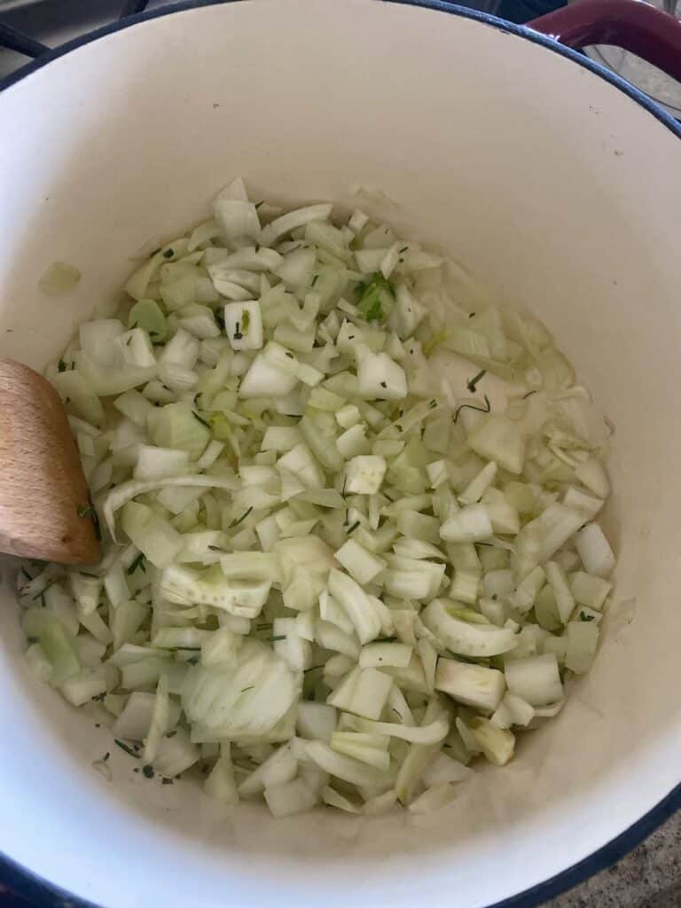 Fennel, onions, and rosemary cooking in olive oil in a Dutch oven.