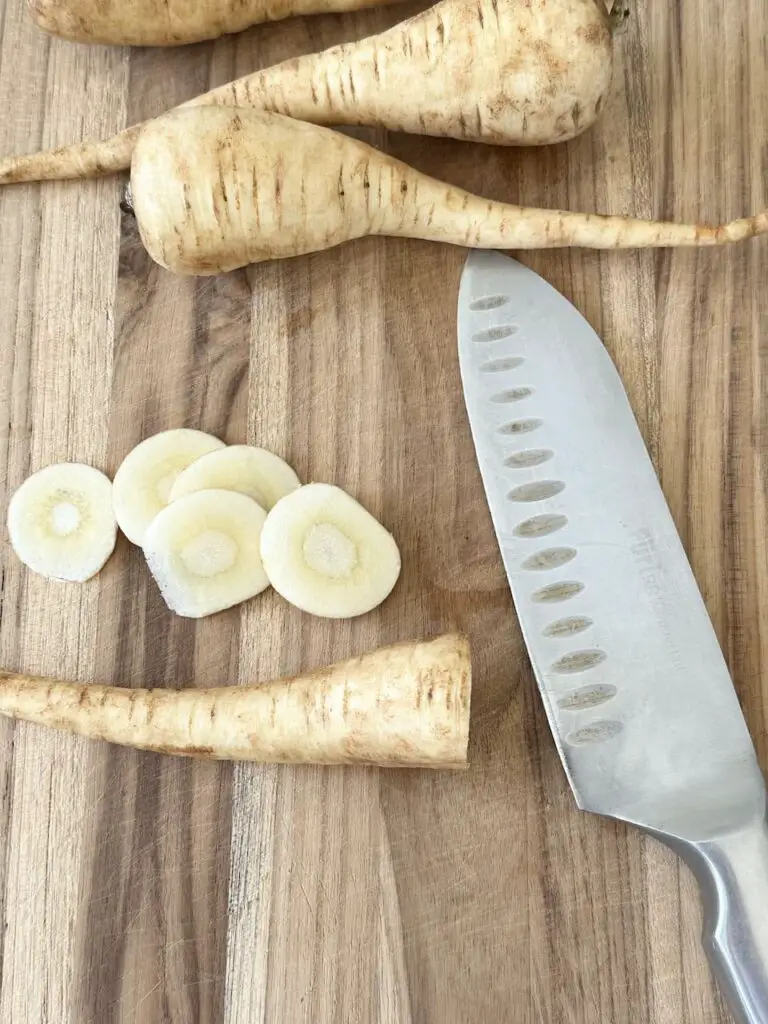 Slicing parsnips on cutting board with sharp knife.