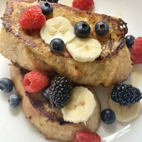 Beautiful plate of vegan French toast topped with syrup, blueberries, raspberries, blackberries, and banana slices.