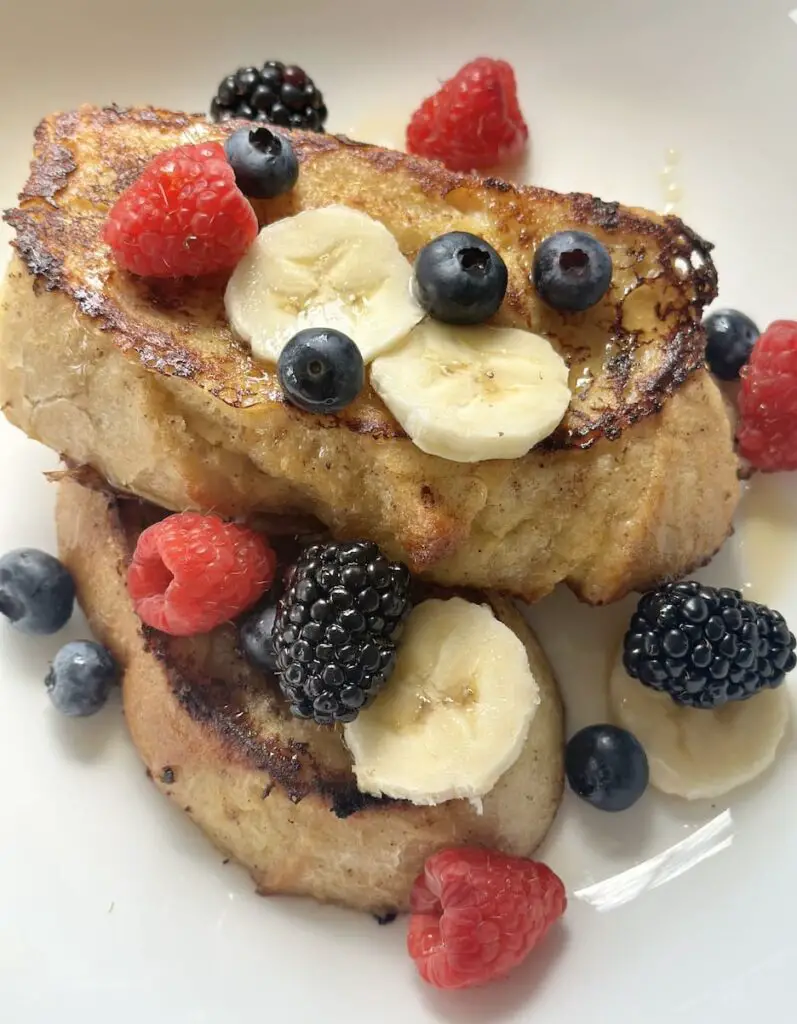 Beautiful plate of vegan French toast topped with syrup, blueberries, raspberries, blackberries, and banana slices.