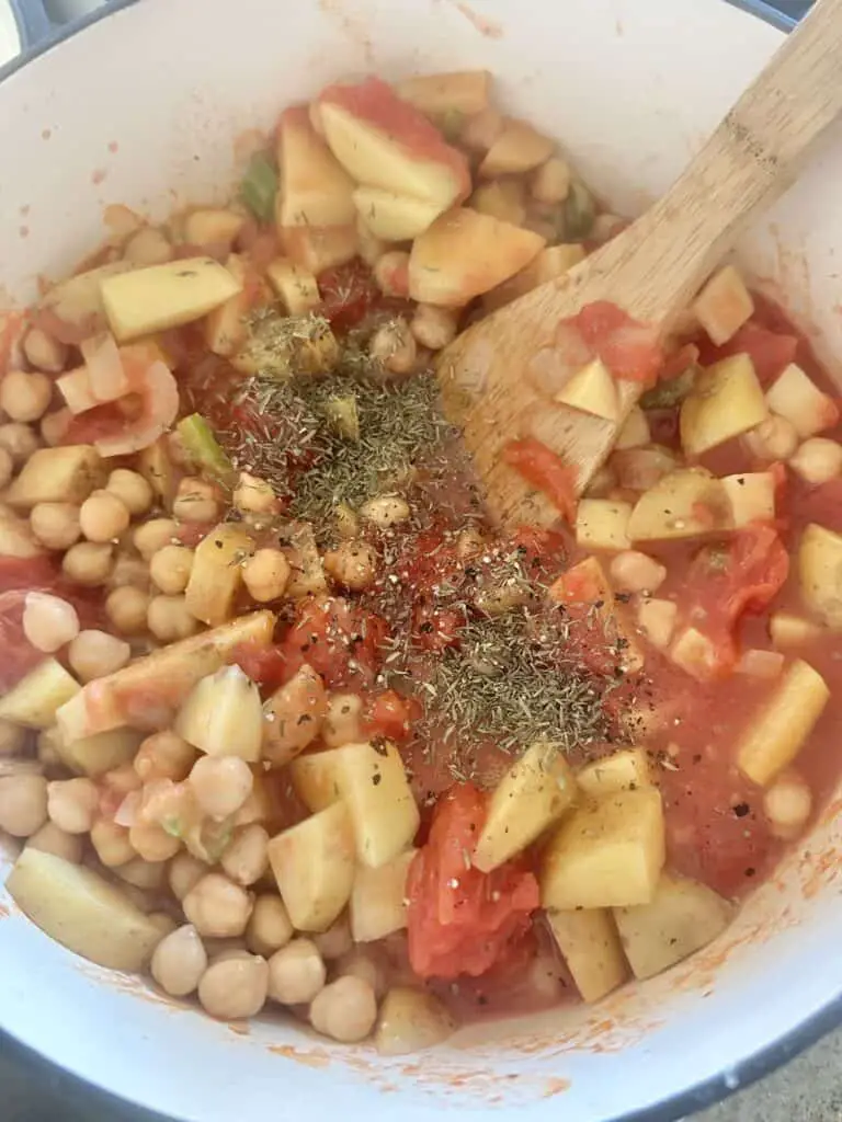 Adding spices and herbs to pot, along with chickpeas.