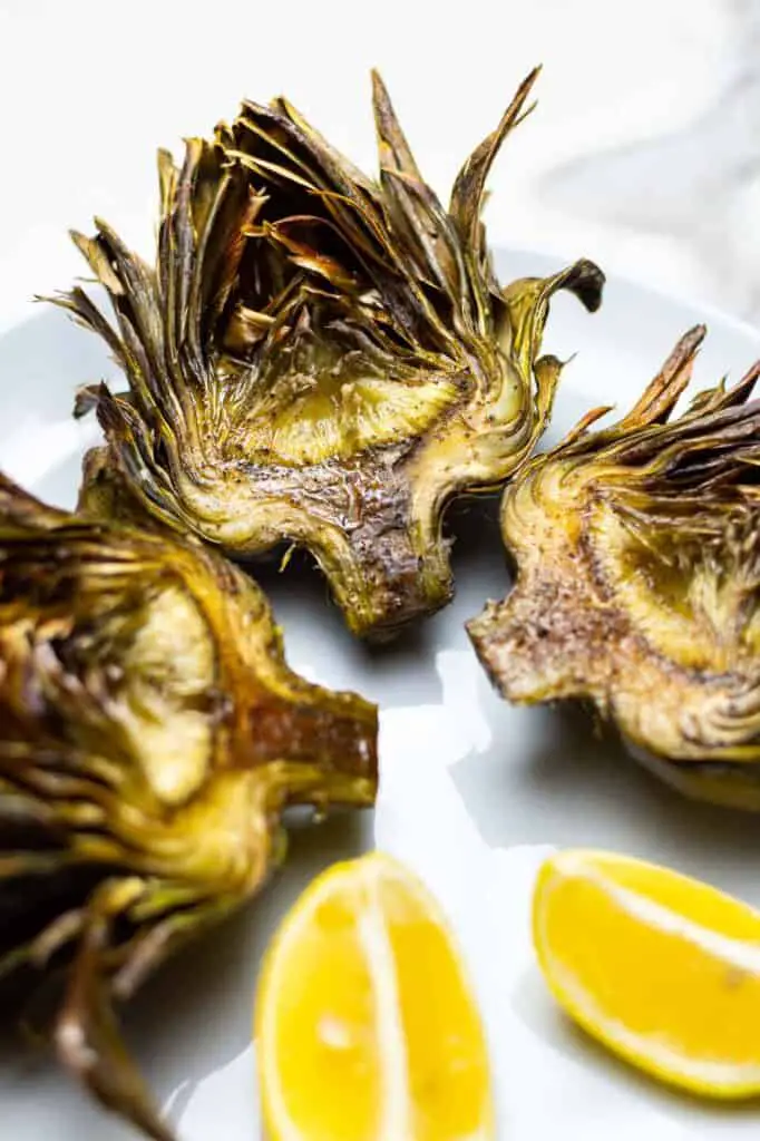Artichokes on a plate with lemon wedges.