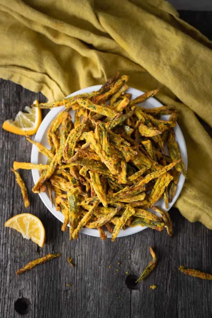 Fried okra in a bowl, spilling over, with lemon wedges.