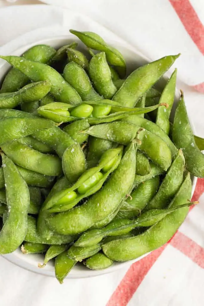 Close up of edamame with some of the shells open so you can see the beans inside.