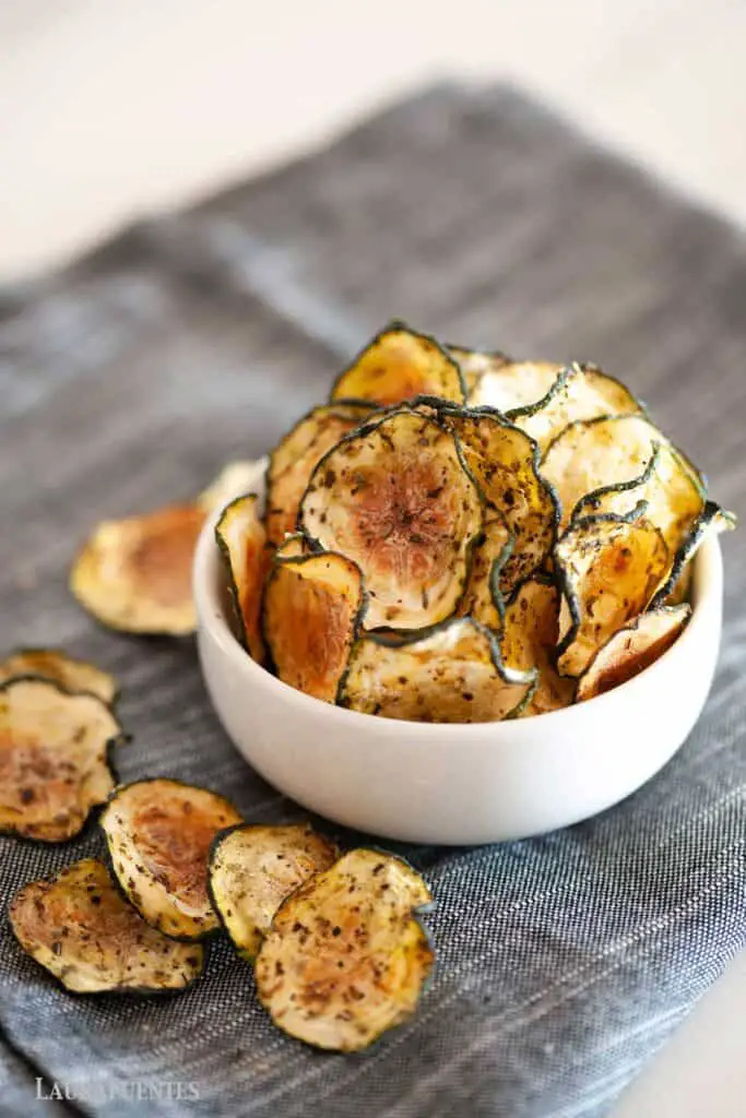 Zucchini chips on a bowl with a few chips on the napkin adjacent.
