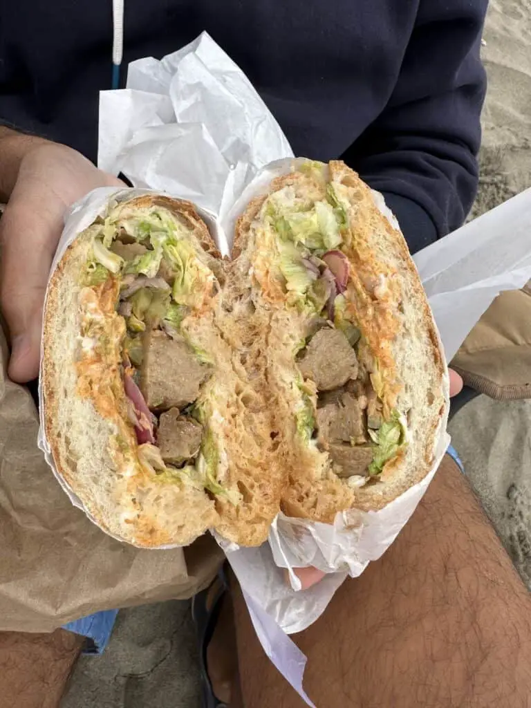 Rhea's vegan sandwich with vegan beef, greens, pickles, and sauces.