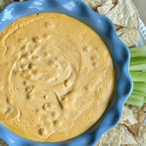 Close up of chickpea buffalo dip in blue pan with tortilla chips and celery.