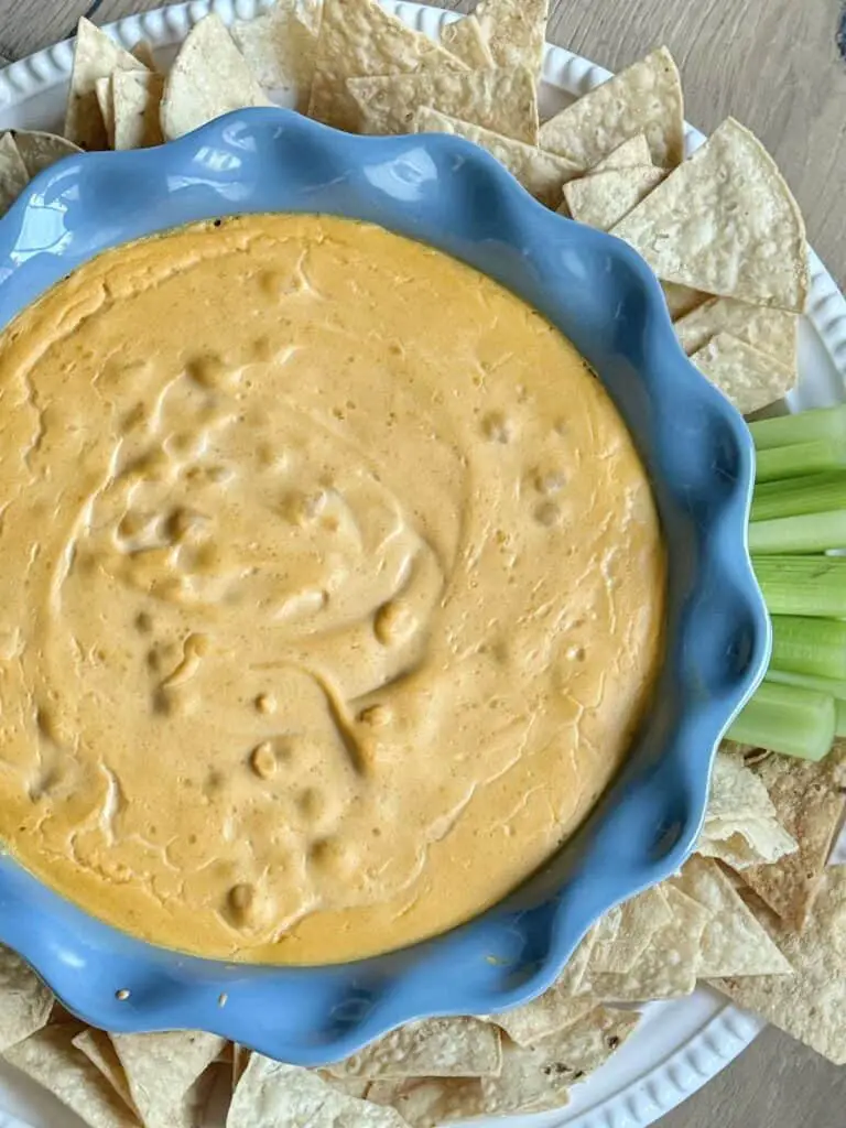 Close up of chickpea buffalo dip in blue pan with tortilla chips and celery.