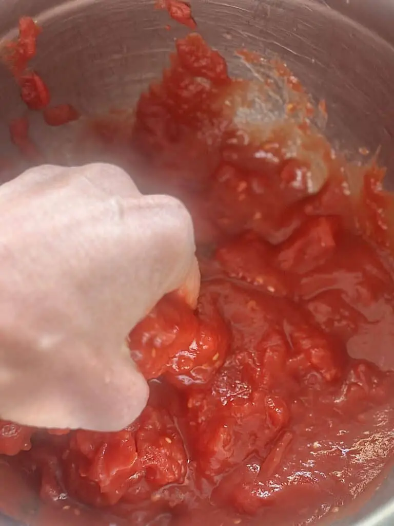 Crushing tomatoes by hand into bowl.