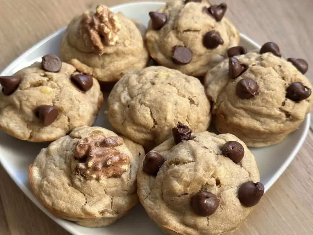 White plate holding an assotrment of vegan muffins: chocolate chip, plain, and banana walnut muffins.